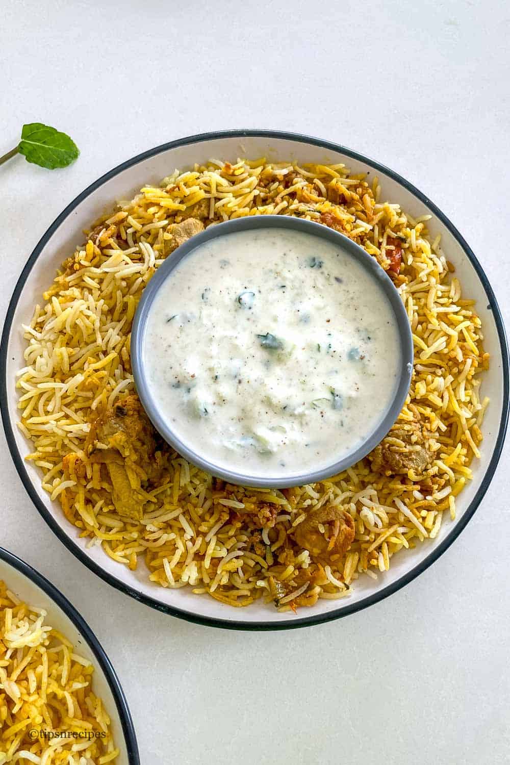 A bowl of cucumber raita along with chicken biryani.