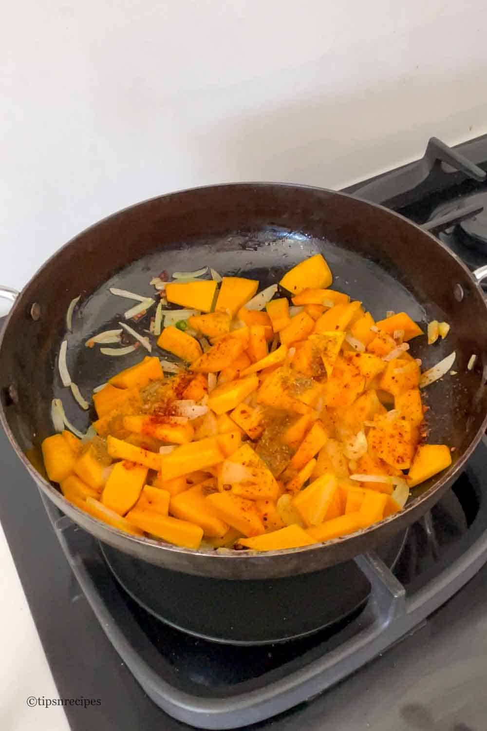 Sautéed pumpkin chunks and onions in a frying pan on stove.