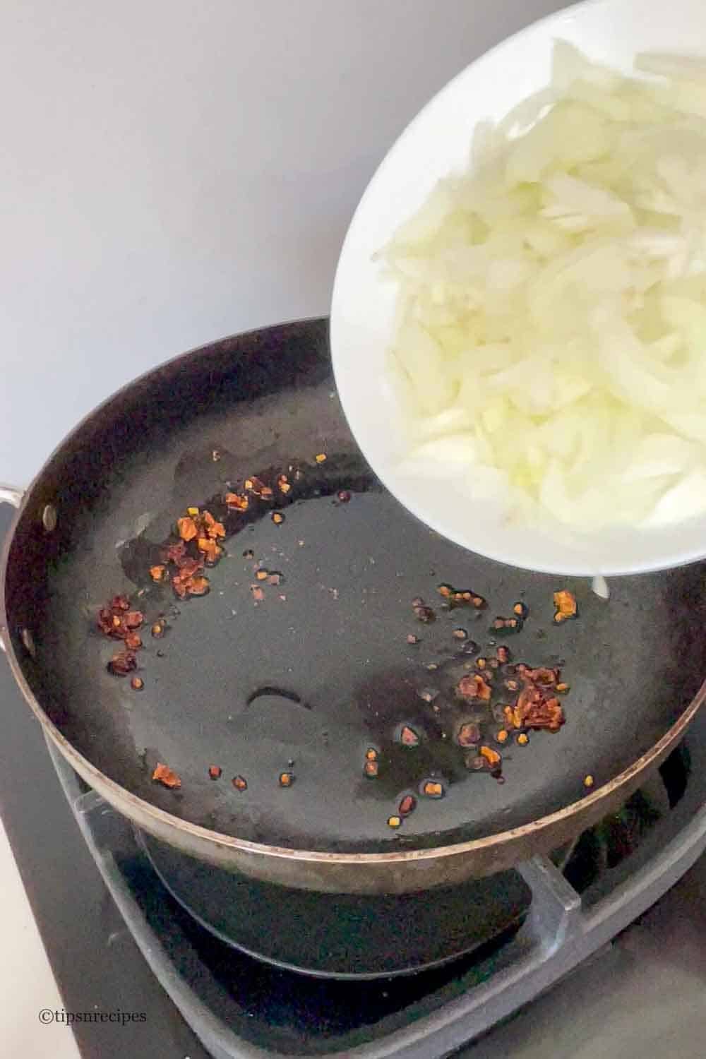 Addding onions to oil in a pan with cumin seeds and dried lentil dumplings.