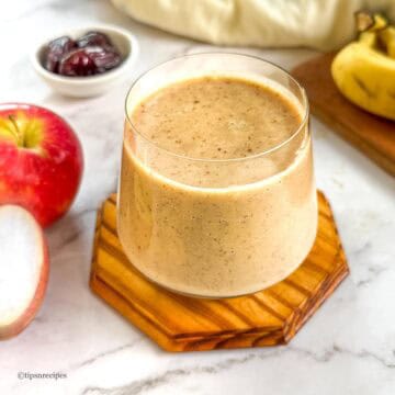 Delicious apple banana smoothie in a glass with fresh fruit around.
