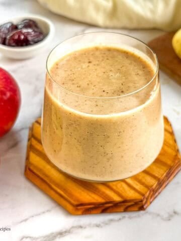 Delicious apple banana smoothie in a glass with fresh fruit around.
