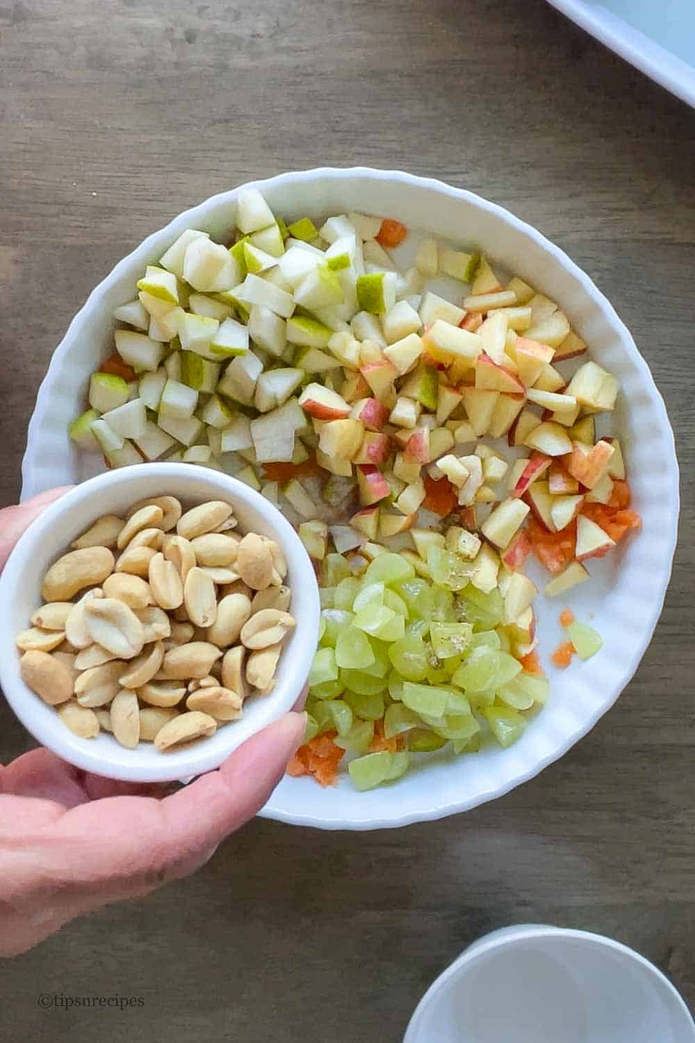 Adding roasted peanuts to the chopped fruits.