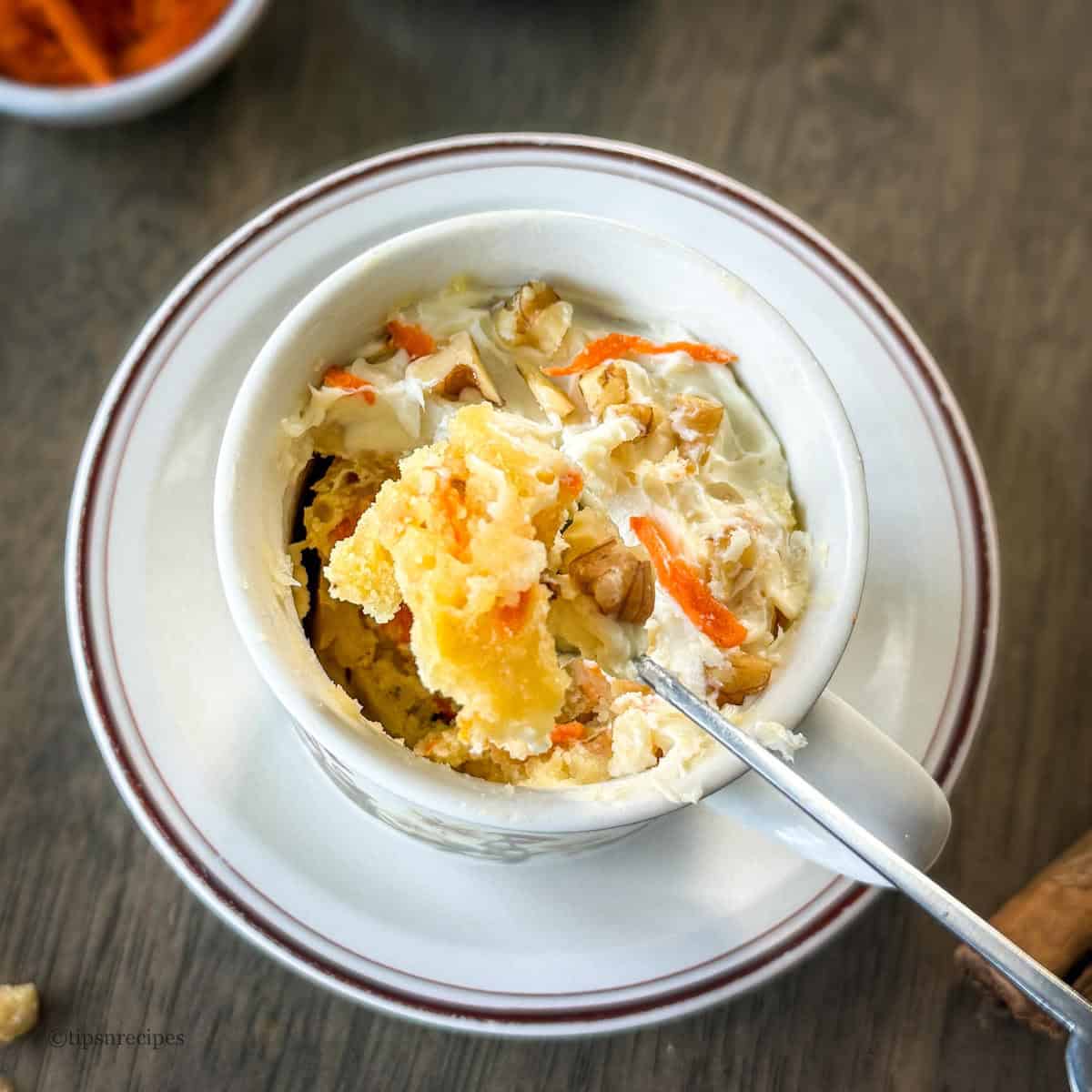 A spoon filled of mini carrot cake prepared in mug with a saucer.