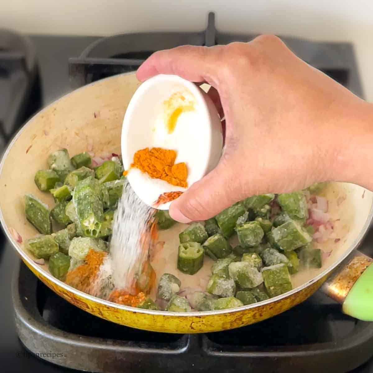 Adding spices to frozen okra into a cooking pan.