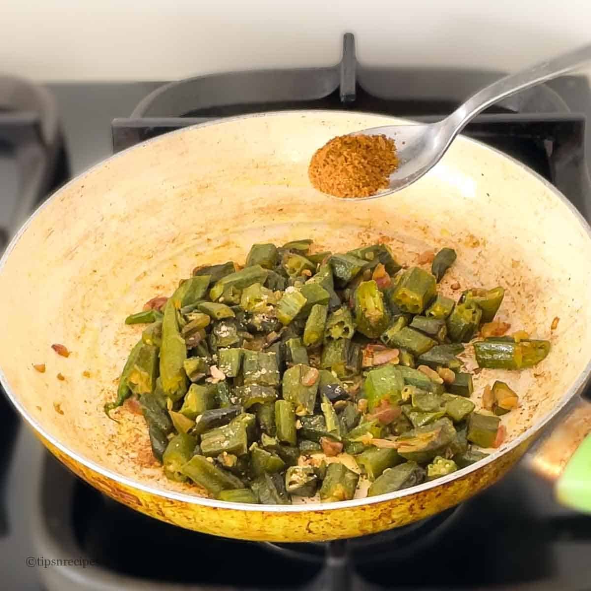 Adding a spoon ful of garm masala into cooked okra.