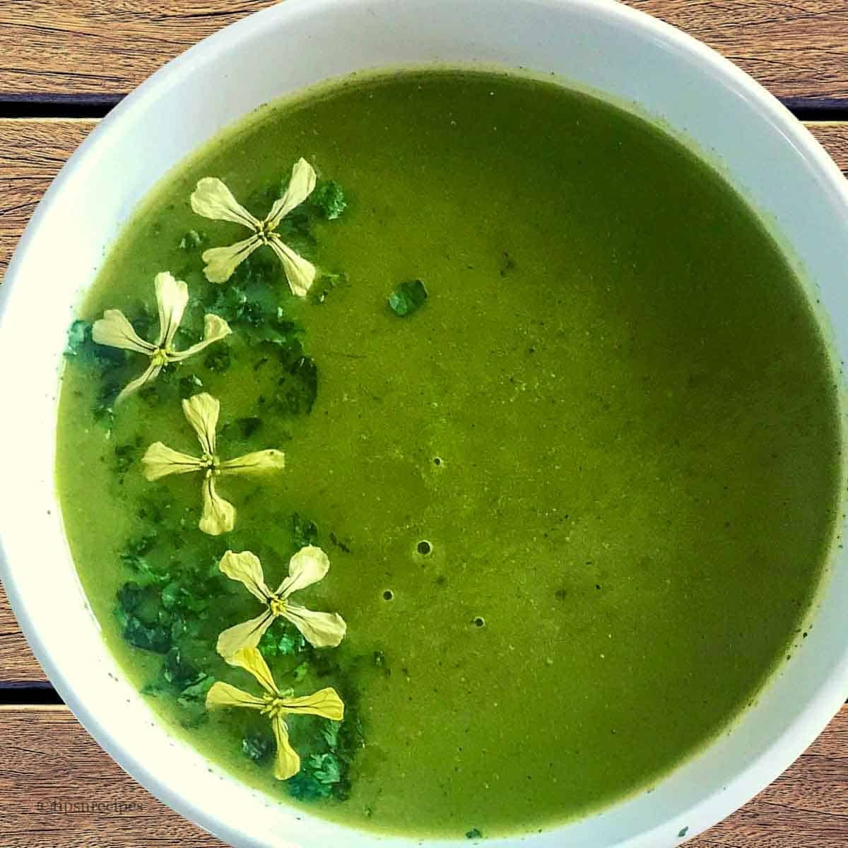 A bowl of green soup with flowers.