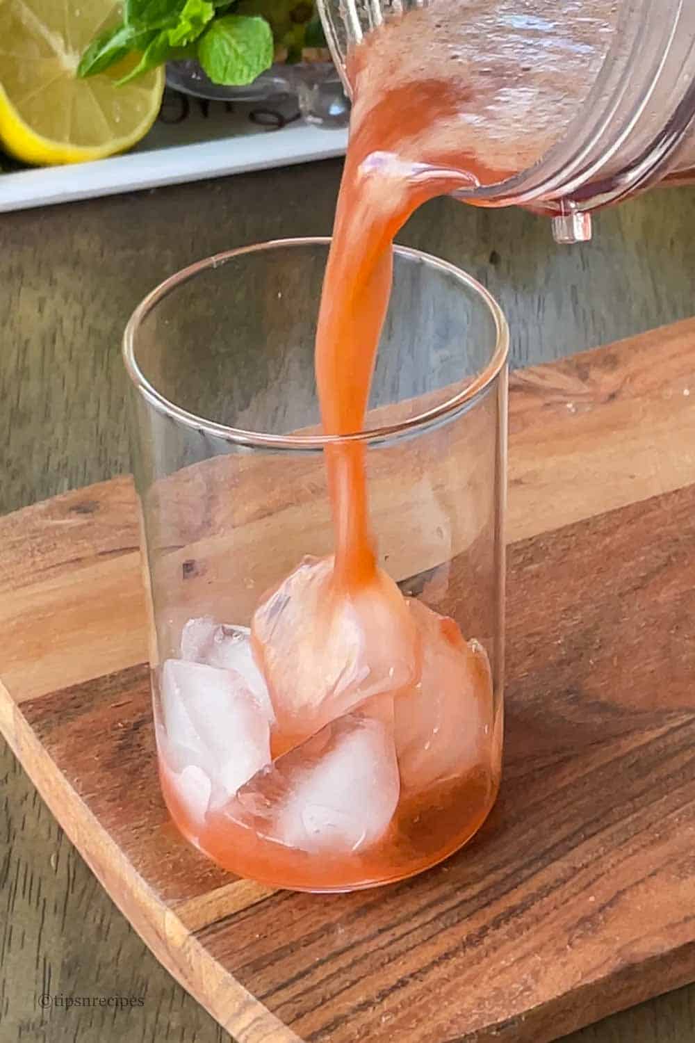Pouring of cooler into glass with ice cubes.