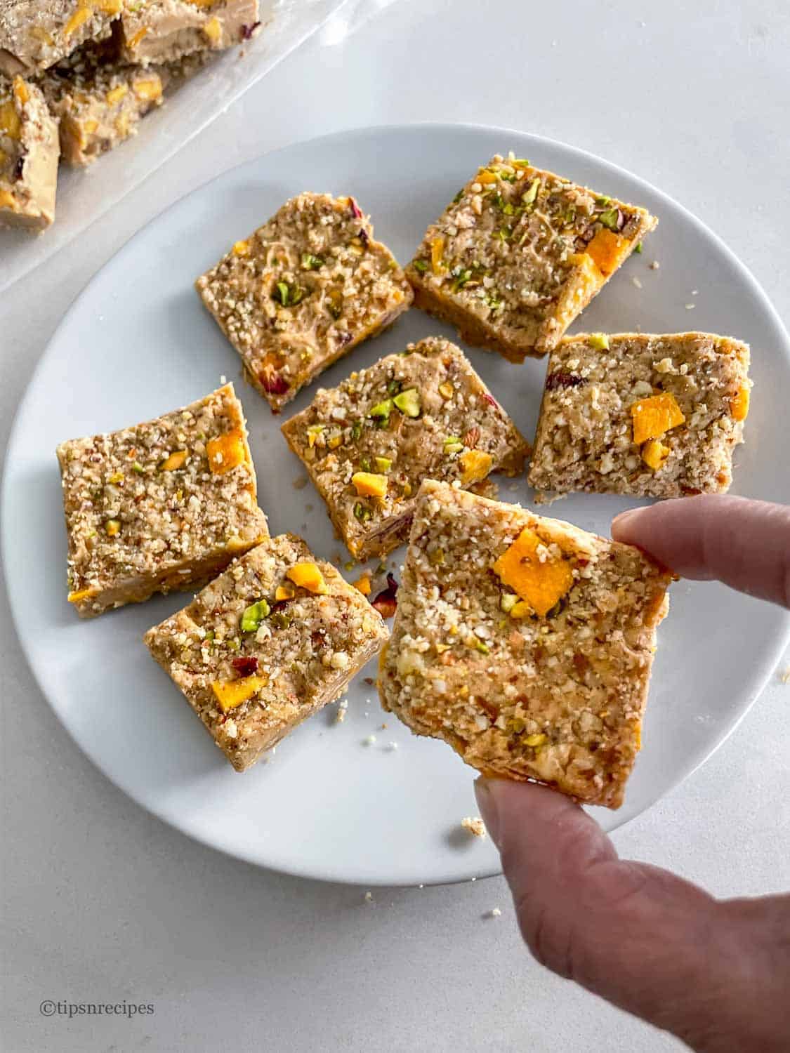 Nutty mango squares with pistachios on a white plate.