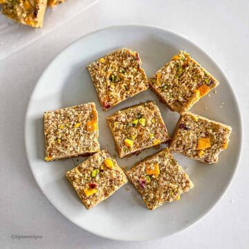 Delicious no-bake nutty mango squares with pistachios and dried fruit on a white plate.