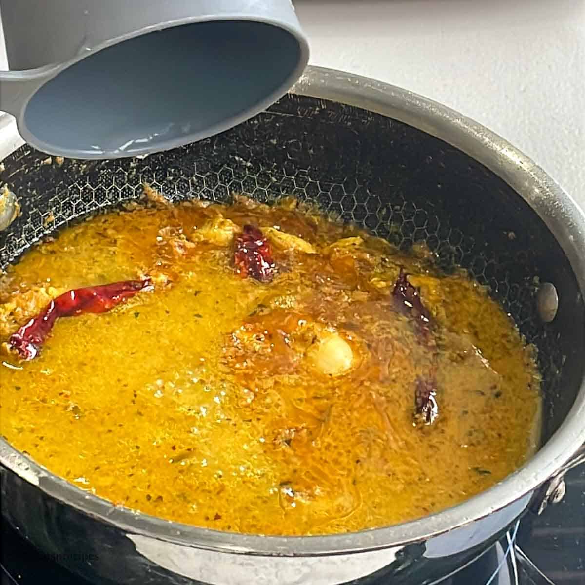 Adding water to butter chicken curry in a skillet.