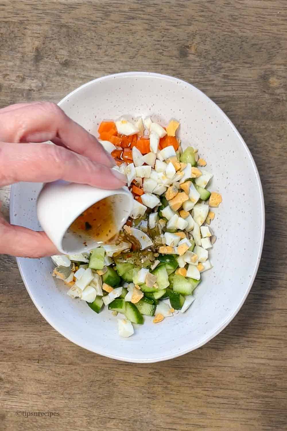 Pouring of salad dressing to a egg veggie salad bowl.