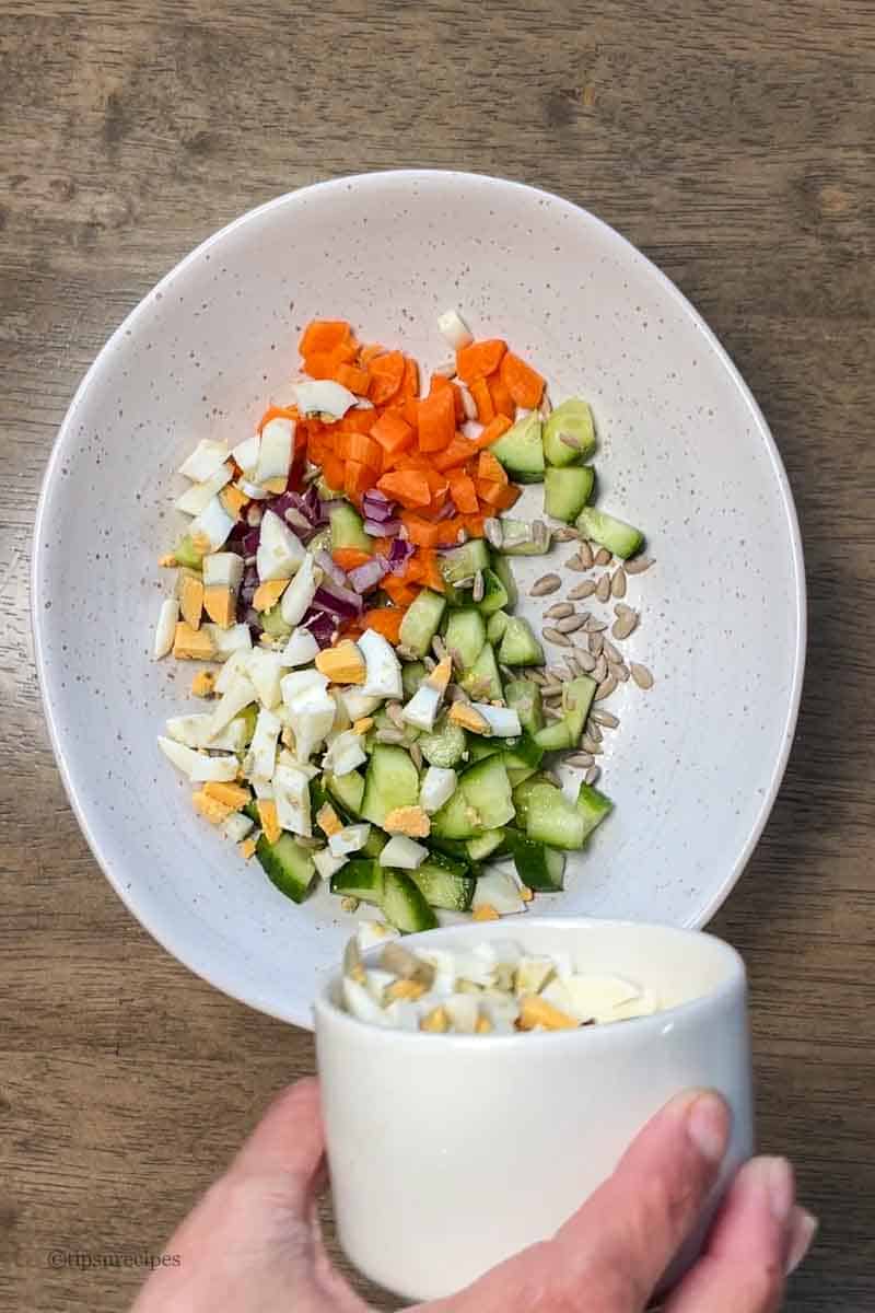 Adding chopped boiled eggs to the vegetables in a bowl.