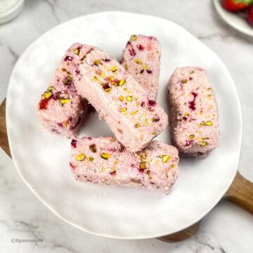 A serving plate of 5 Strawberry Coconut bars placed on wooden platform.