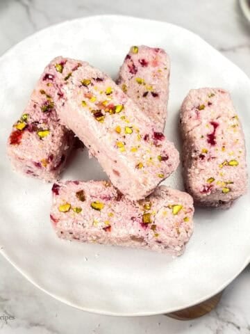 A serving plate of 5 Strawberry Coconut bars placed on wooden platform.