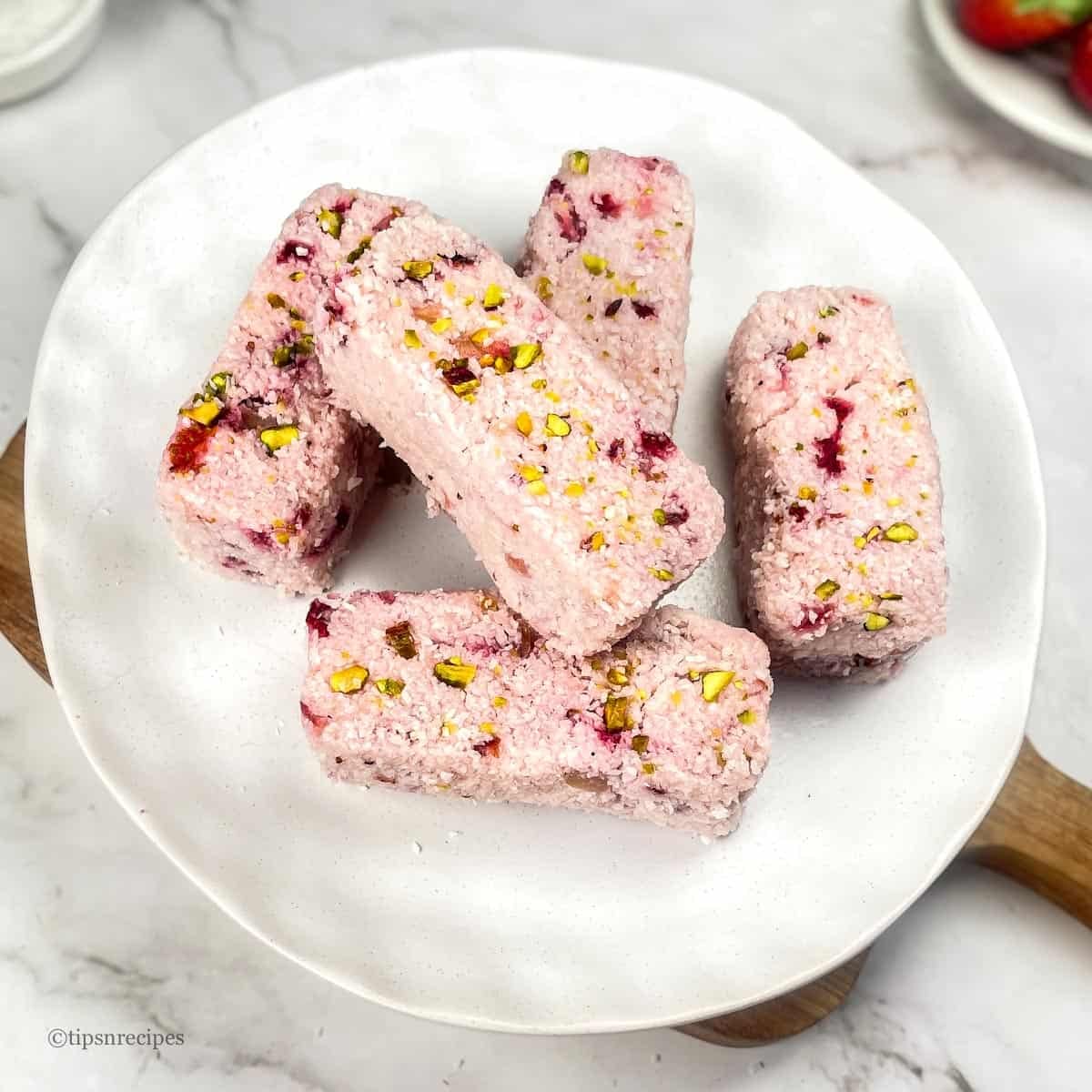A serving plate of 5 Strawberry Coconut bars placed on wooden platform.