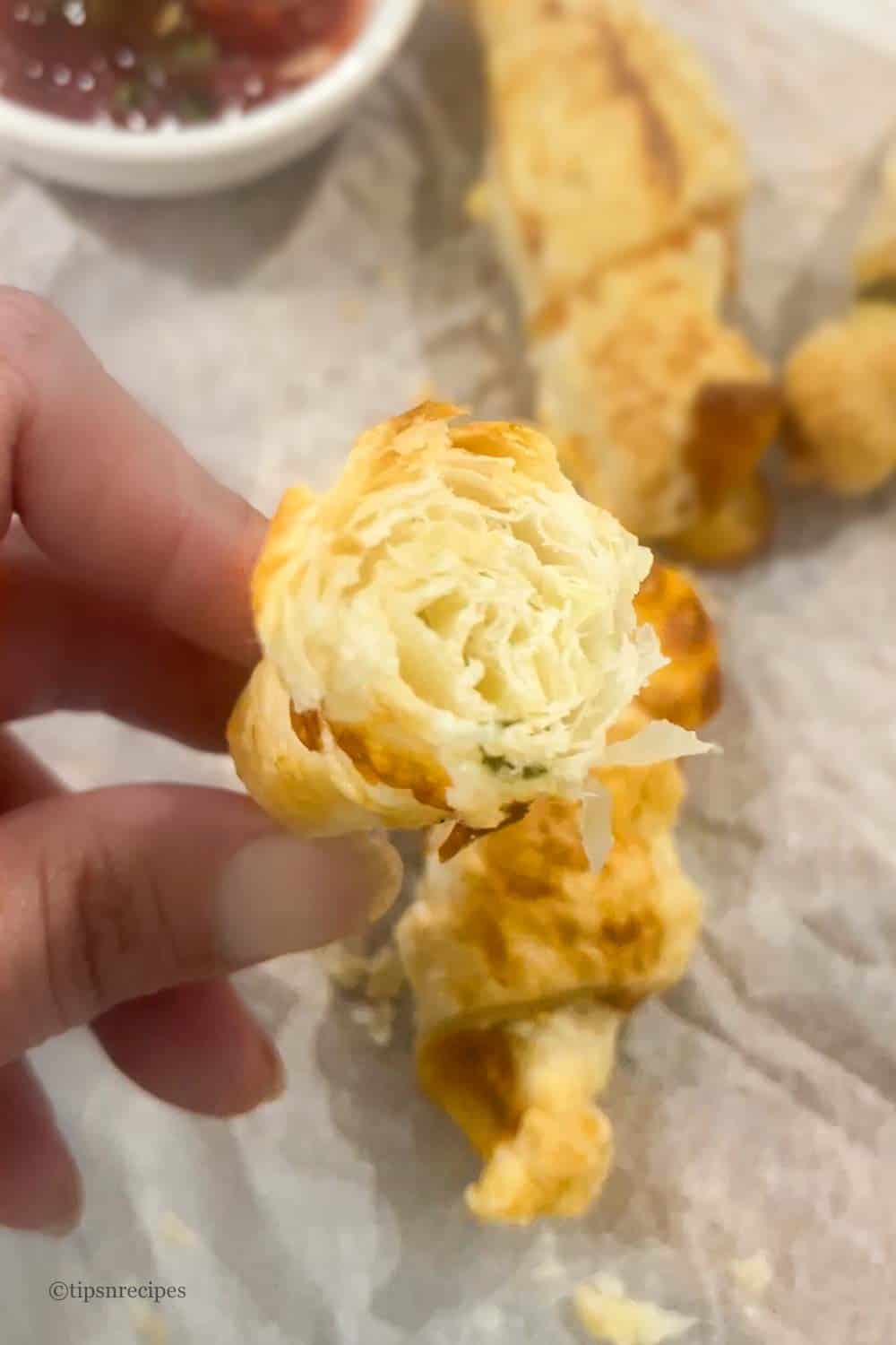 Hand showing flaky, buttery land cheesy layered texture of mini croissants.