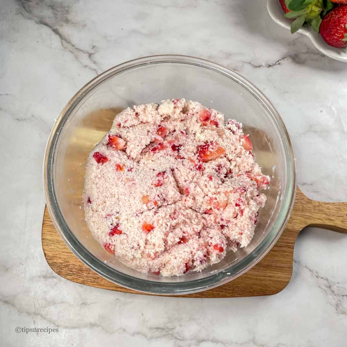 A mixing bowl with coconut, strawberries and condensed milk.