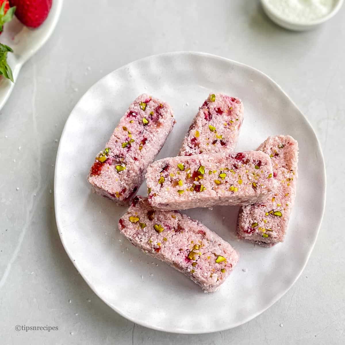 A serving plate of bars made with strawberry and coconut.