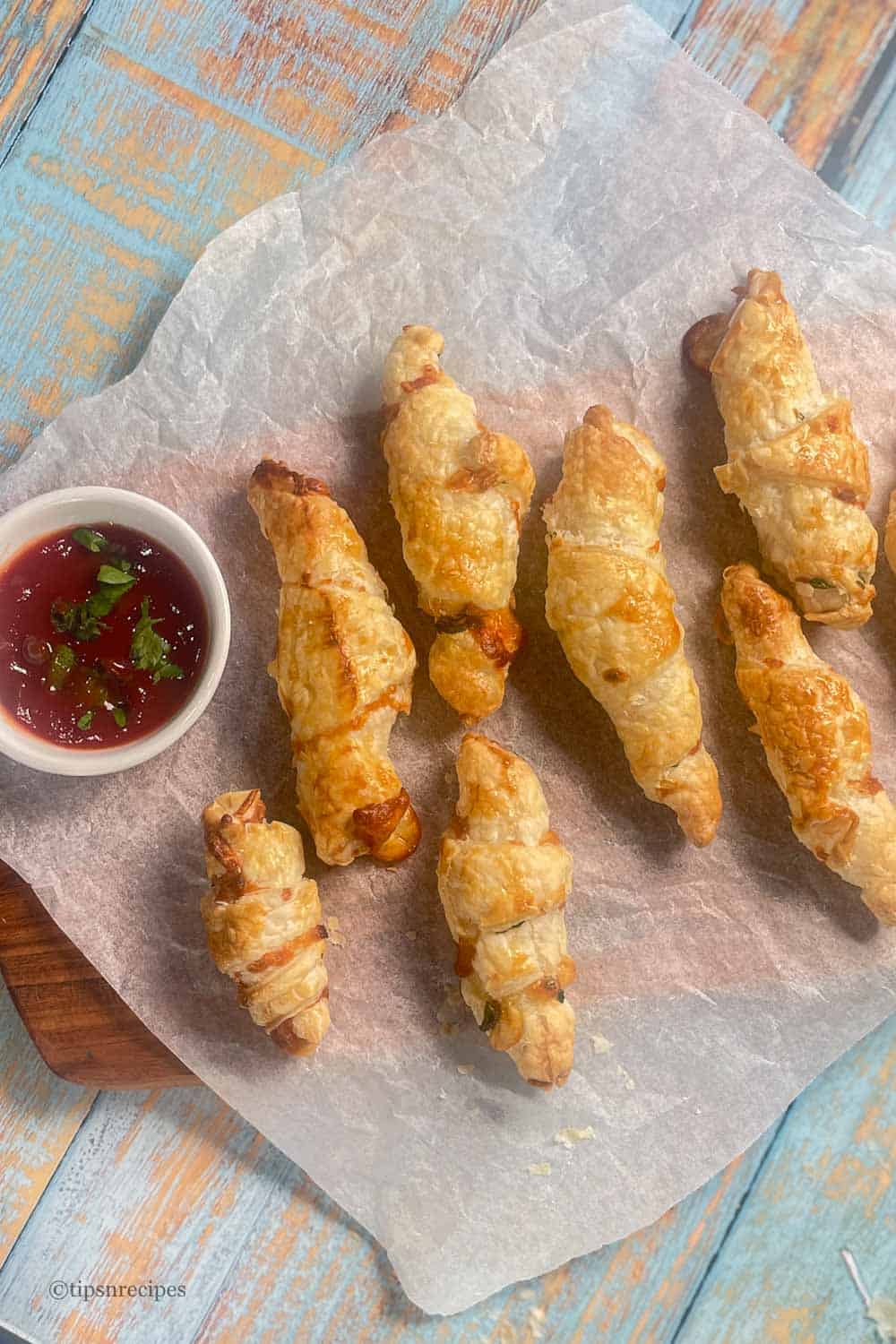 Mini cheesy crossiants on parchment paper with a dipping sauce.