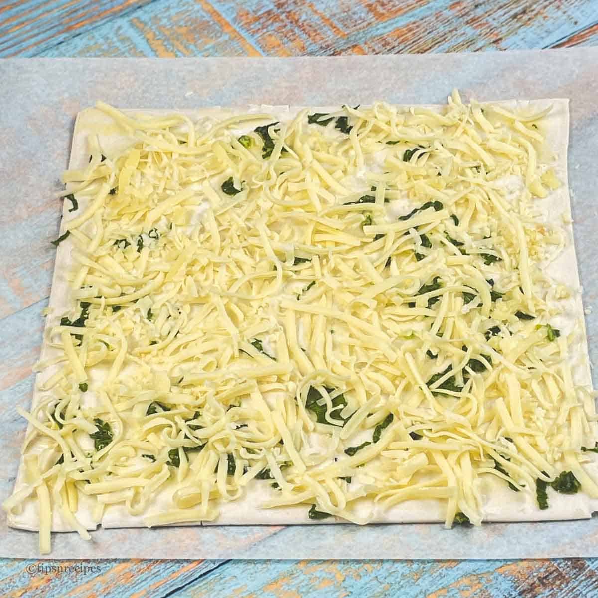 Mozerella cheese with parsley spreaded over puff pastry sheet.