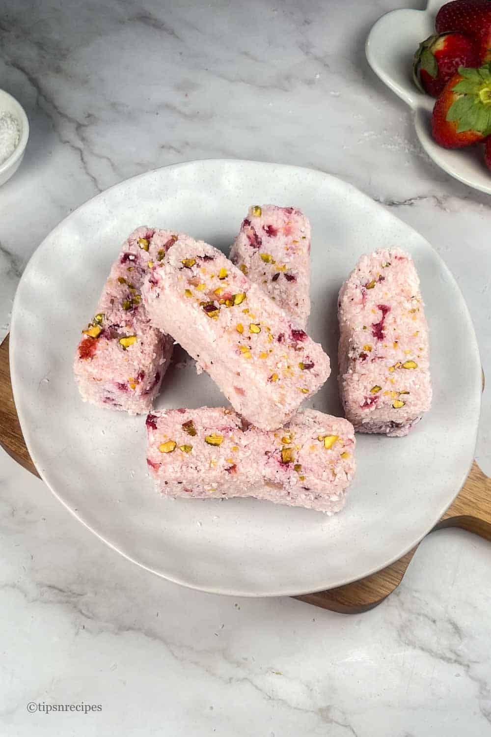 A plate of no bake bars prepared with fresh strawberries and coconut.
