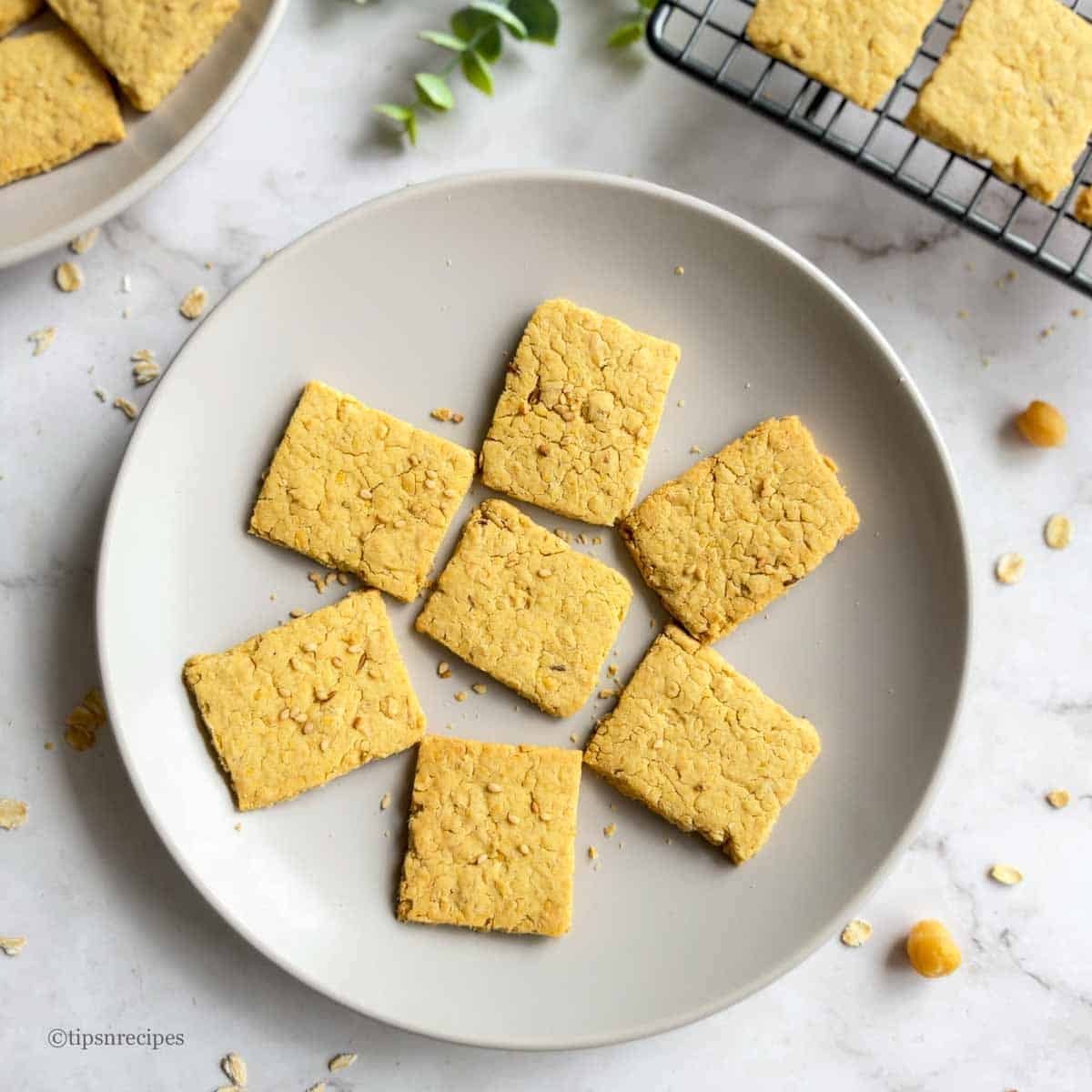 A plate of air fryer chickpea and oat crackers with some crackers on a rack.